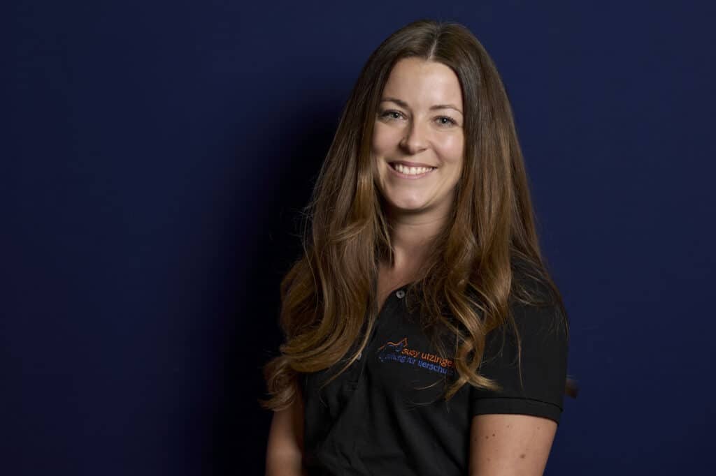 Jana Bauer im schwarzen SUST-Poloshirt vor dunkelblauem Hintergrund