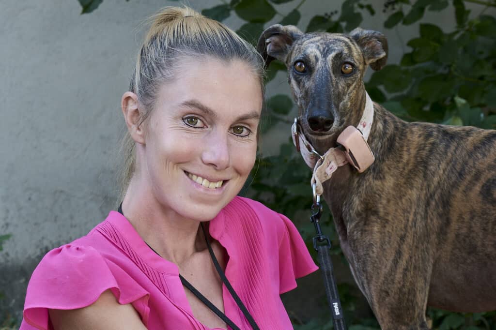 Meret Schneider lächelt in die Kamera, hinter ihr steht ihr Windhund